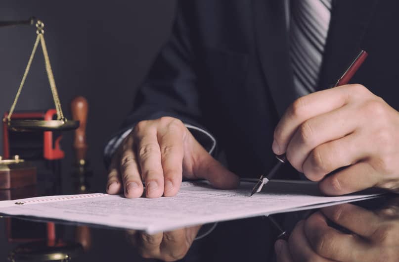 Un avocat en costume signant un document à un bureau.